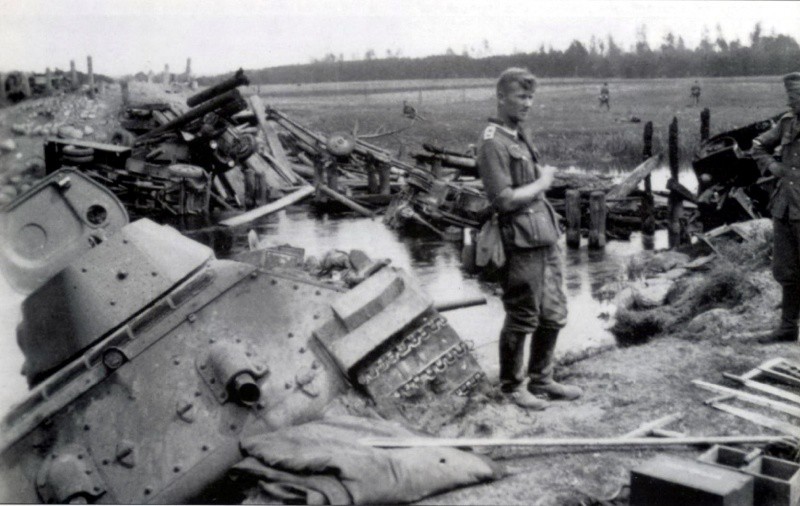 Немецкий фельдфебель возле советского танка Т-34 на разбитой переправе через речку Зельвянка. На переднем плане танк Т-34 образца 1941 года, в реке утопленный танк Т-34 образца 1940 года с пушкой Л-11. вов, фото