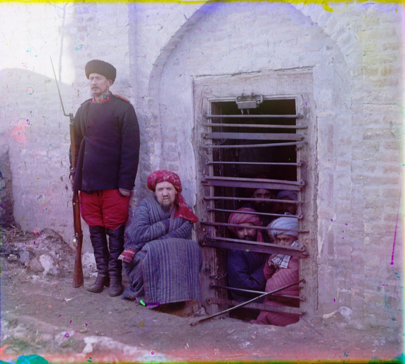 Zindan prison, with inmates looking out through the bars and a guard with Russian rifle, uniform, and boots, Central Asia. (between 1905 and 1915)